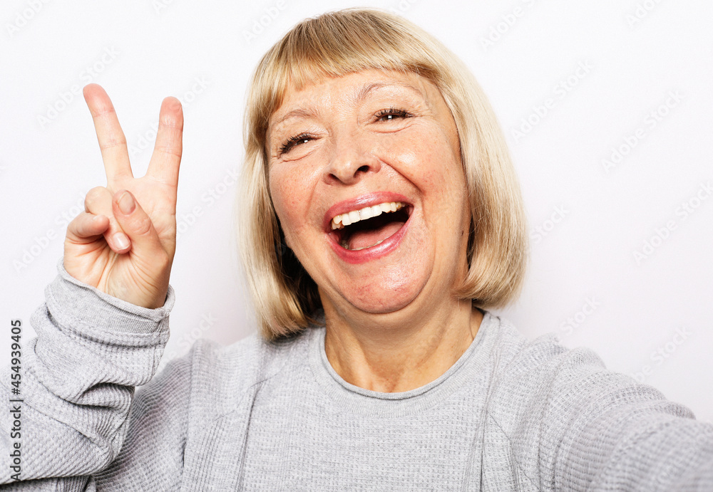 Elderly woman making selfie with peace sing and smilling. Portrait of handsome expressive grandmother wearing casual. Elderly woman making selfie with peace sing and smilling. Portrait of handsome expressive grandmother wearing casual.