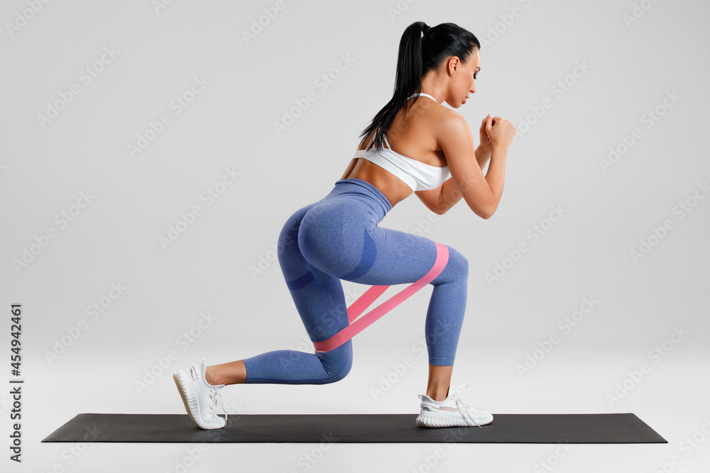 Fototapeta premium Fitness woman doing exercise for glute with resistance band on gray background. Athletic girl working out