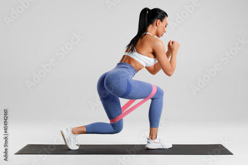 Fototapeta Naklejka Na Ścianę i Meble -  Fitness woman doing exercise for glute with resistance band on gray background. Athletic girl working out