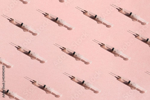 A pattern of a medical syringe on a pink paper background with a shadow, a concept of healthcare, vaccination, a new vaccine against the coronavirus 2019-nCoV or COVID-19. Flat layout, 