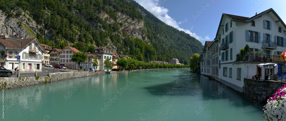 vu panoramique sur un petit village Suisse le long d'un pont fleurie au bord d'une rivière turquoise sous un ciel bleu 