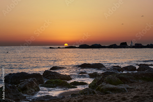 sailing boat on the horizon near to the sun at sunset barcelona