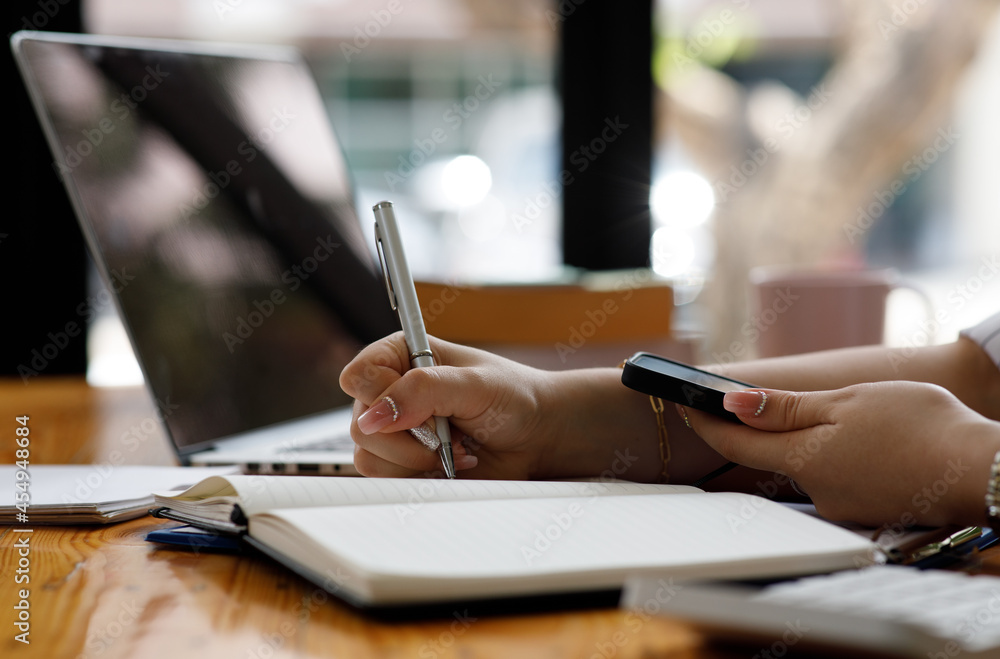 Close up of Casual woman using smartphone, working on laptop computer from home office Close up of Casual woman using smartphone, working on laptop computer from home office