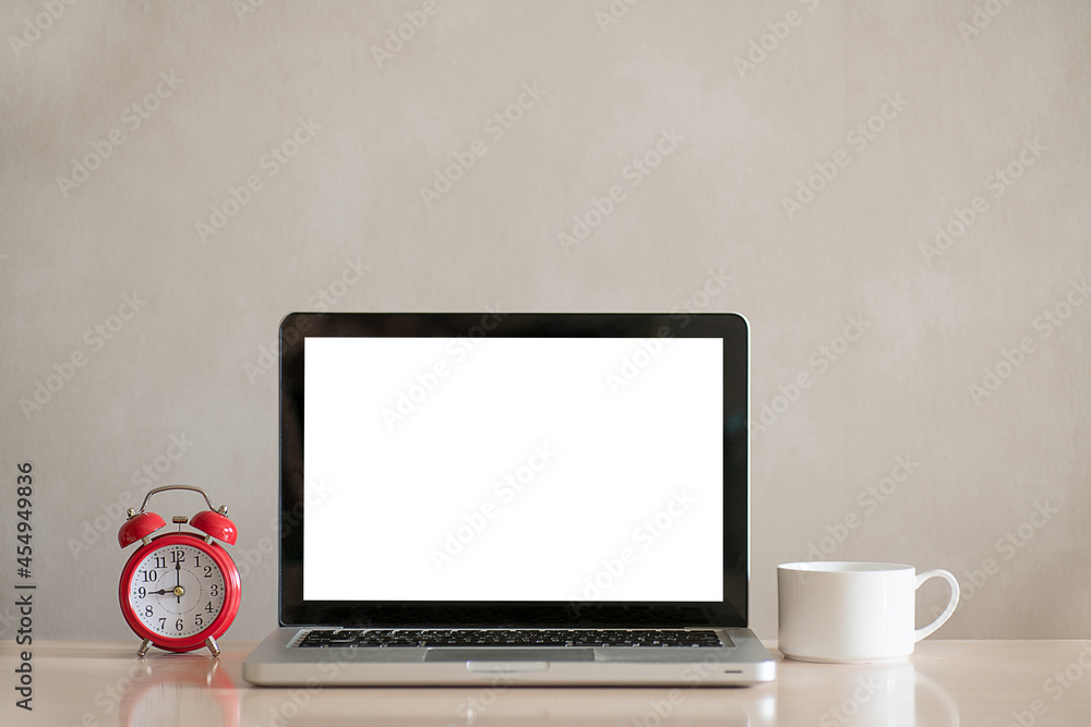 Laptop, red alarm clock and white cup on wooden table on grey wall background. Workplace with copy space on laptop screen Laptop, red alarm clock and white cup on wooden table on grey wall background. Workplace with copy space on laptop screen