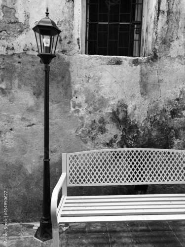 Wooden chair lonely resting with street antique lamp in front of old concrete wall, in black and white tone. Grey scale.