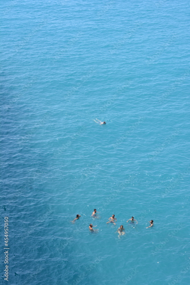 Una persona nuota distante dal gruppo di amici e amiche in mezzo al mare facendo snorkeling  e nuotando nel mare calmo. Ripresa aerea con drone dall'alto.
