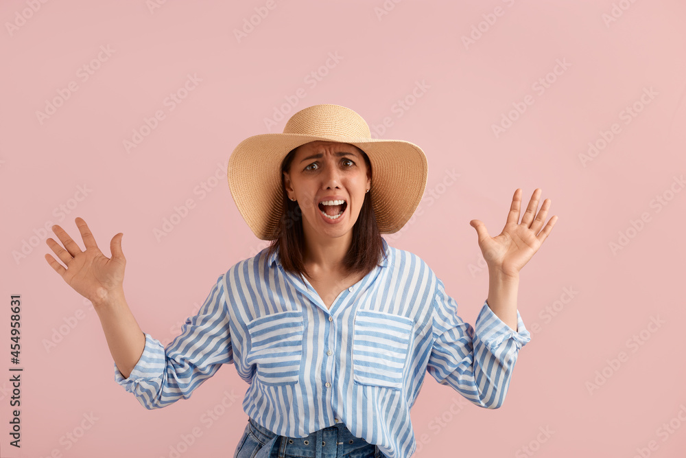 Scared alarmed annoyed woman with dark hair screams loudly in fear, keeps mouth wide open, keeps palms raised, wears straw hat, striped shirt, jeans, on pink background. Summer emotions concept. Scared alarmed annoyed woman with dark hair screams loudly in fear, keeps mouth wide open, keeps palms raised, wears straw hat, striped shirt, jeans, on pink background. Summer emotions concept.