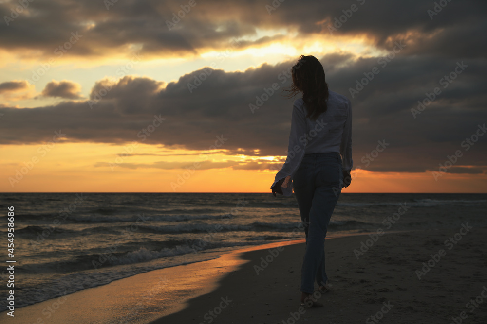 Woman walking on sandy beach during sunset, back view