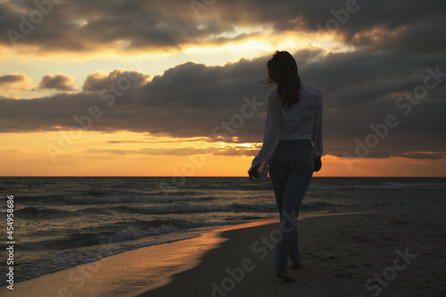 Woman walking on sandy beach during sunset  back view