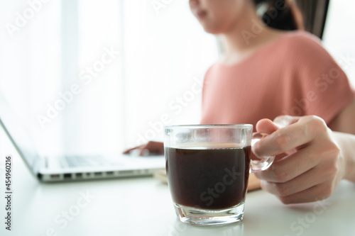 Beautiful young Asian woman holding a cup of hot black coffee on the table while working. 