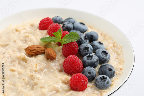 Tasty oatmeal porridge with raspberries, blueberries and almond nuts in bowl on white background, closeup