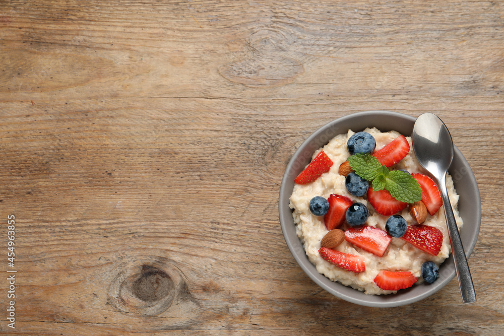 Tasty oatmeal porridge with berries and almond nuts in bowl on wooden table, top view. Space for text