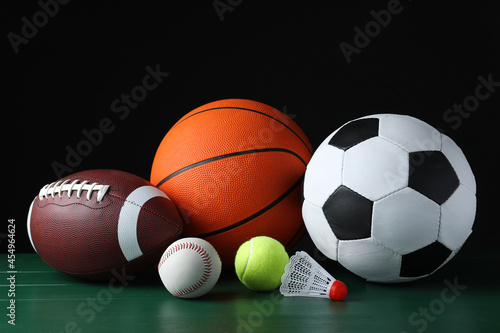Set of different sport balls and shuttlecock on green wooden surface