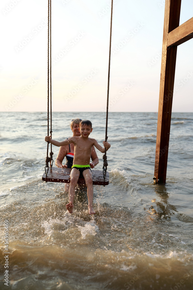 Woman rocks happy child on swing in Sea of Azov