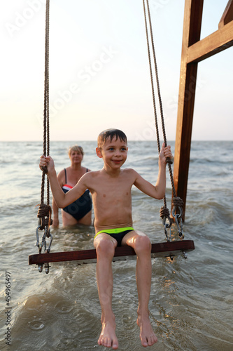 Woman rocks happy kid on swing in Sea of Azov