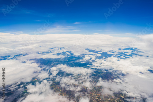 Aerial view scene of the mountain, meadow and abundant rice which hiding under white fluffy clouds and blue bright sky background.