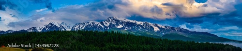 Panoramic view of plain among hills and mountains under white fluffy clouds in blue sky at sunny day