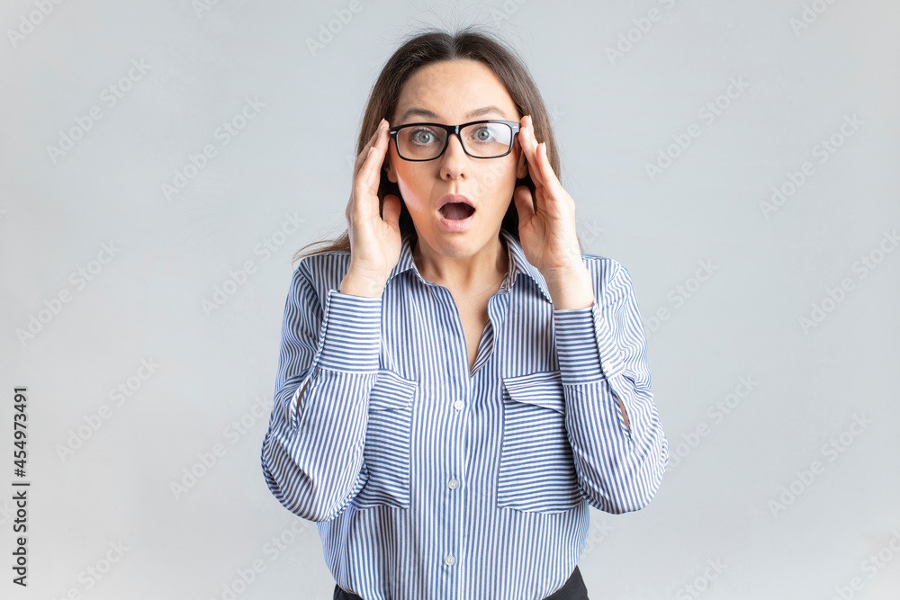Surprised young businesswoman in eyeglasses standing in front of gray background Surprised young businesswoman in eyeglasses standing in front of gray background