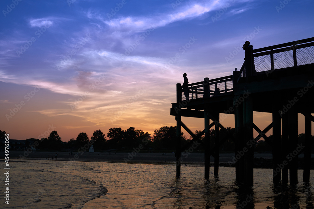 Silhouette of a person standing at the end of a pier overlooking the water as the sun goes down