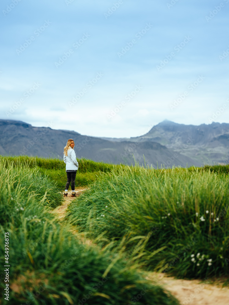 Woman in jacket walks along path near grass and mountains in Iceland Woman in jacket walks along path near grass and mountains in Iceland
