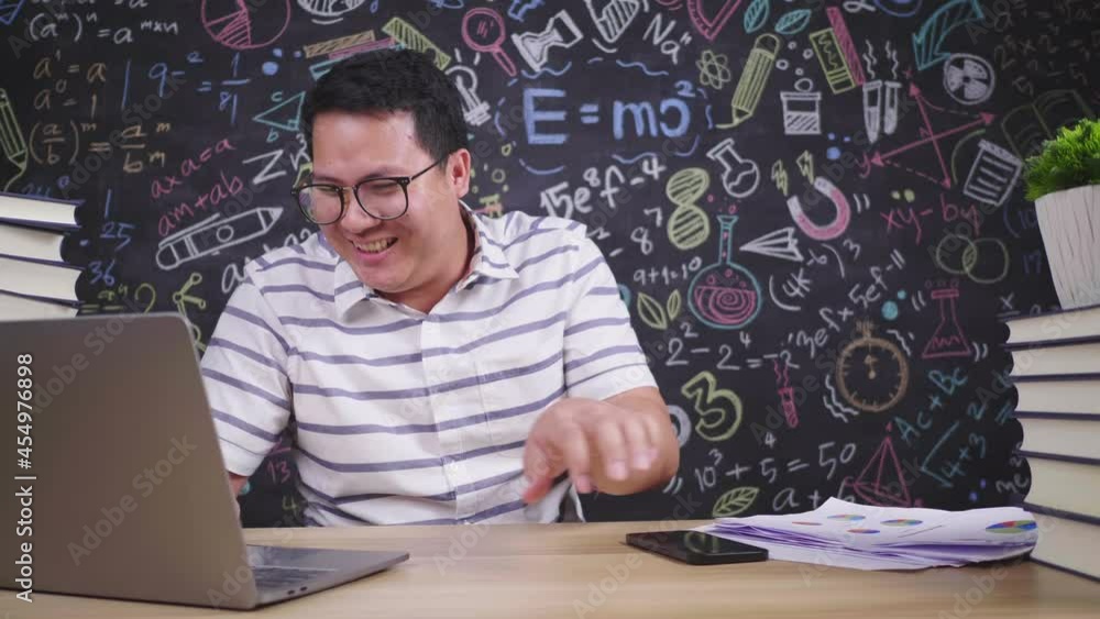 Enjoy teacher glasses man working and singing while sitting at desk in classroom. Cheerful male teacher typing laptop. E-learning, learn from home, education. Enjoy teacher glasses man working and singing while sitting at desk in classroom. Cheerful male teacher typing laptop. E-learning, learn from home, education.