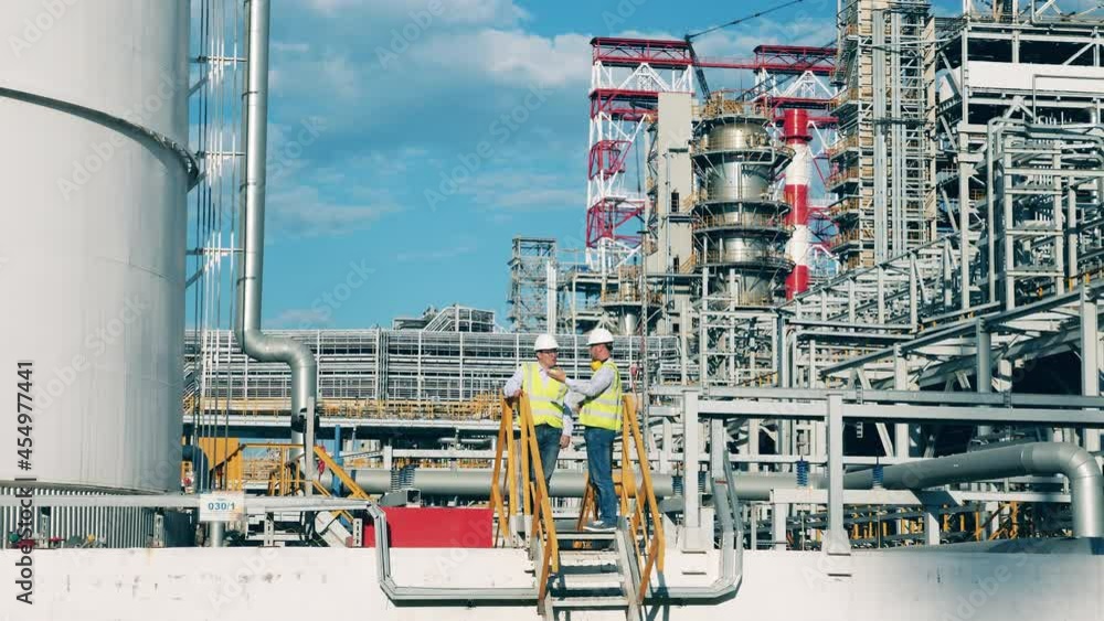 Premises of the oil refinery with industrial workers talking Premises of the oil refinery with industrial workers talking
