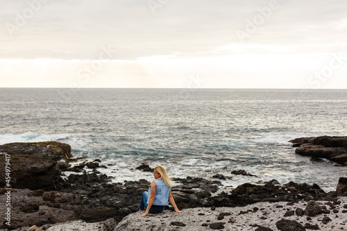 Women on volcanic rocks and blue ocean with waves, white foam and volcanic rocks. Canary Islands. The magnificent coast of the Atlantic Ocean