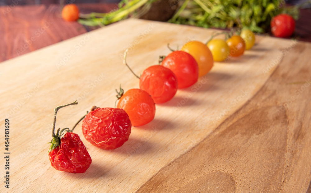 Cherry tomatoes, cherry tomatoes lined up from greenest to rotting through ripe on a wood, dark background, selective focus. Cherry tomatoes, cherry tomatoes lined up from greenest to rotting through ripe on a wood, dark background, selective focus.