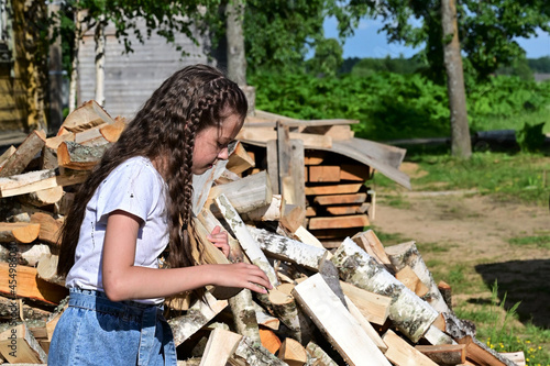 beautiful girl with long hair in white shirt puts firewood in pile. Concept of harvesting firewood for winter. Firewood for fireplace. Close-up