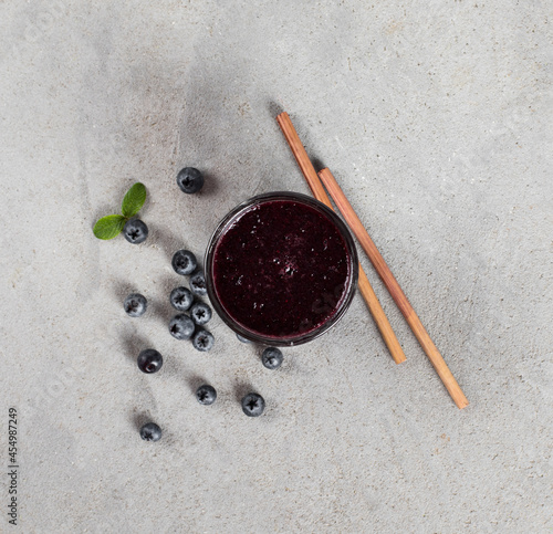 Blueberry smoothie in glass with bamboo straw on a light gray background top view