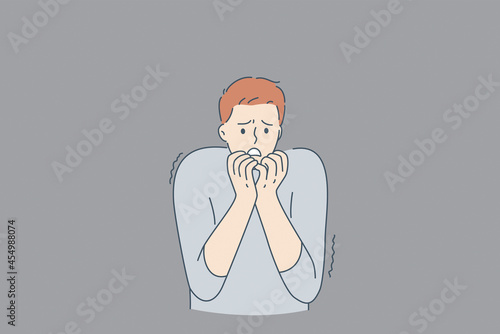 Mental health and inner fears concept. Young stressed man cartoon character standing biting nails feeling bad with ghosts at wall from inside fears vector illustration 