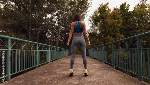 Rear view of a sportive woman standing on a bridge in the middle of nature. Brown tinted