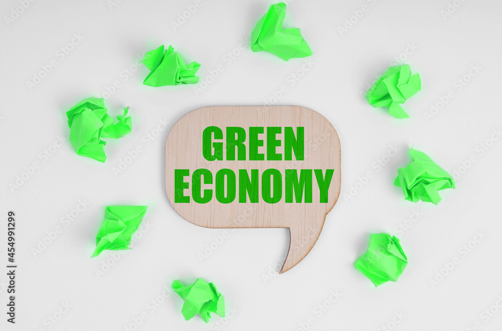 On a white background, there are crumpled green pieces of paper and a wooden sign with the inscription - Green economy On a white background, there are crumpled green pieces of paper and a wooden sign with the inscription - Green economy