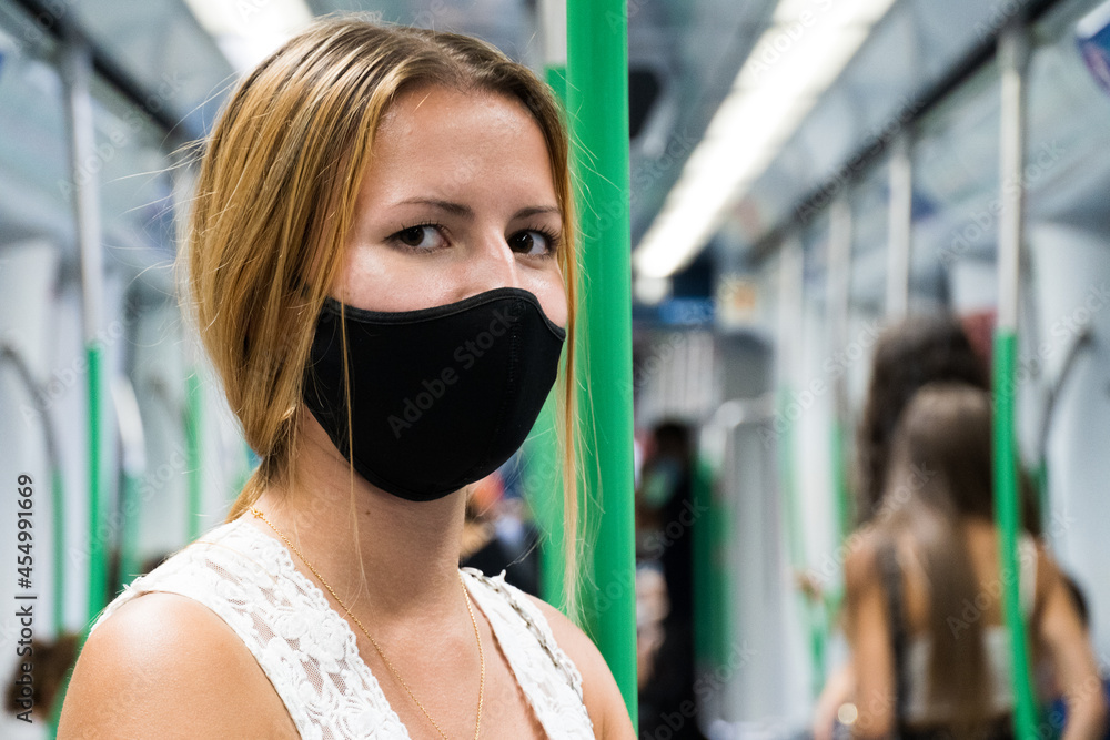 Portrait of a young blonde white girl dressed in a white tank top and a black mask in the subway