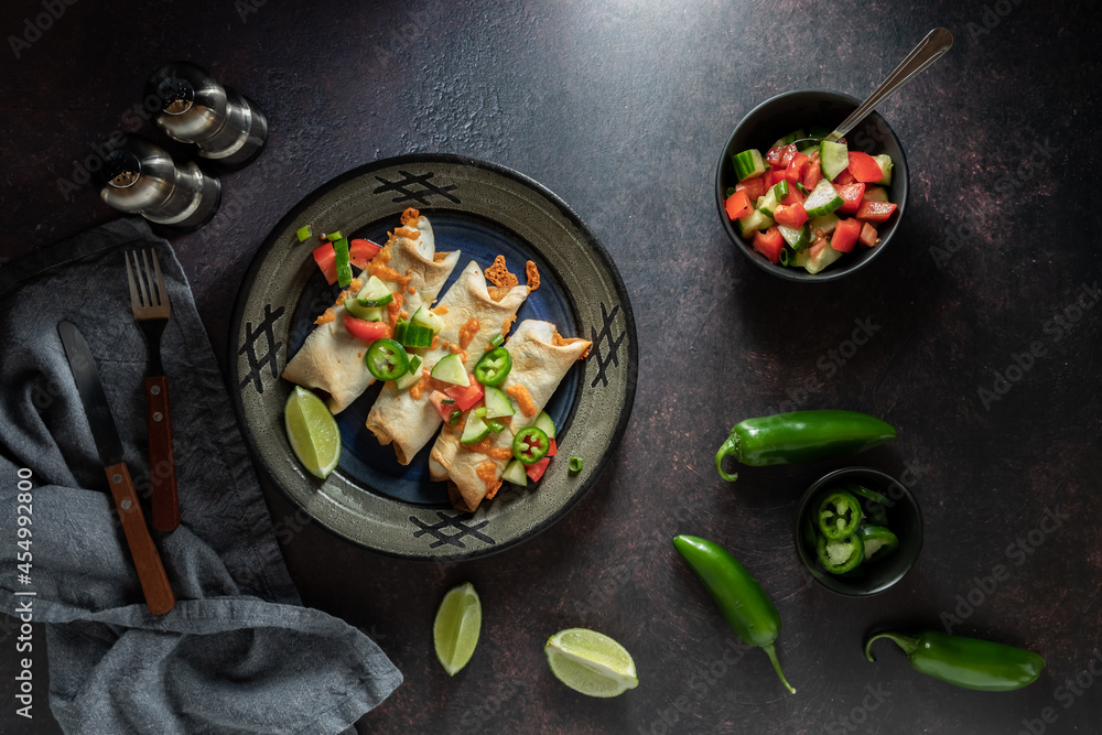 Top down view of taquitos topped with homemade tomato and cucumber salsa and served with jalapeno peppers. Top down view of taquitos topped with homemade tomato and cucumber salsa and served with jalapeno peppers.