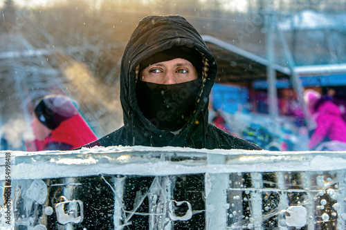 A man in a black sunny winter, in black clothes and a mask on the street / sun rays