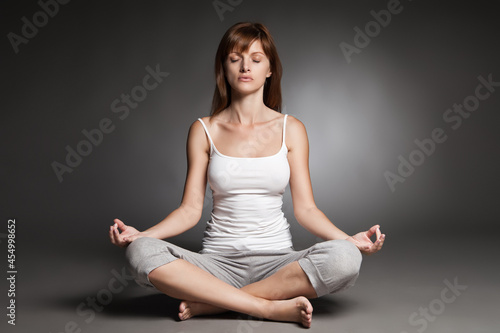 Young woman doing yoga against dark background