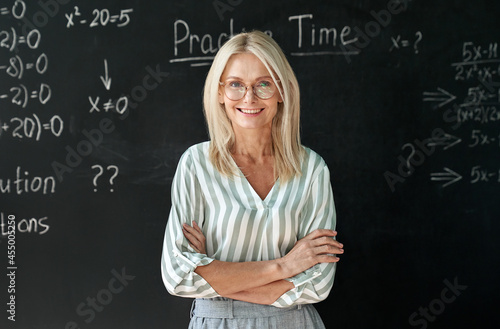 Fotografia Happy smiling middle aged woman mature high school education math teacher or college professor wearing glasses standing at blackboard background