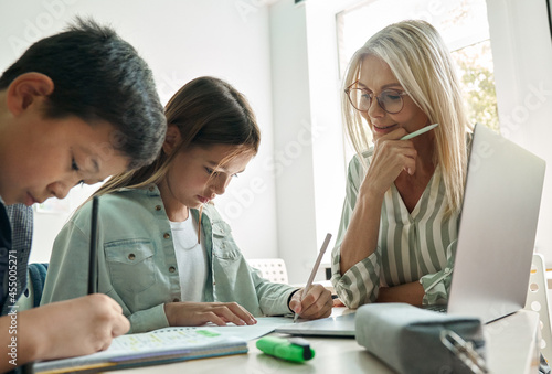 Photography Female teacher or tutor diverse kids children Asian boy and Latin girl students with homework learning sitting at desk in classroom