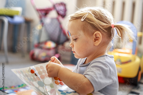 Portrait of a little lovely girl. Cute toddler sticks stickers on herself. Lovely blonde baby in a blue shirt.