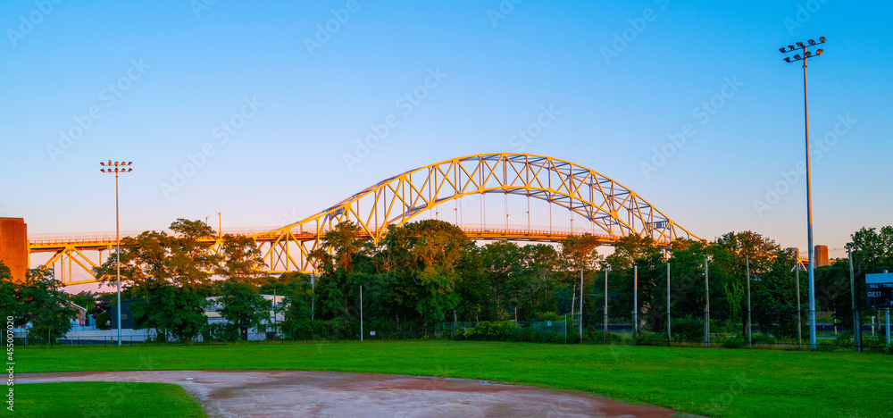 Fototapeta premium Youth baseball field with the view of the arched Sagamore Bridge illuminated by the rising sun