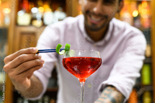 close-up of glass with red drink that barman accurate decorate with orange peel