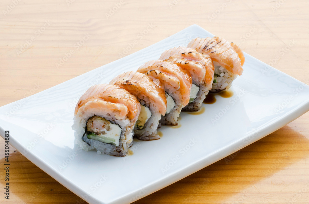 Sushi rolls with teriyaki salmon on white plate on wooden table Sushi rolls with teriyaki salmon on white plate on wooden table