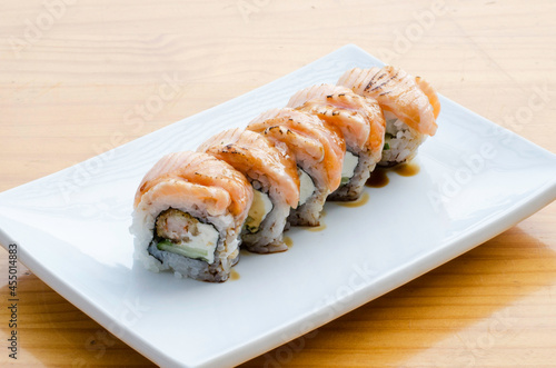 Sushi rolls with teriyaki salmon on white plate on wooden table