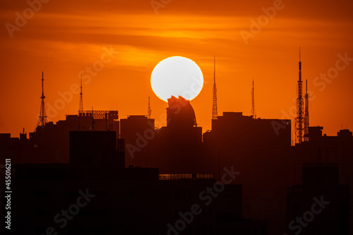 Por do Sol na grande cidade entre prédios e torres de transmissão à sombra com o grande Sol ao fundo