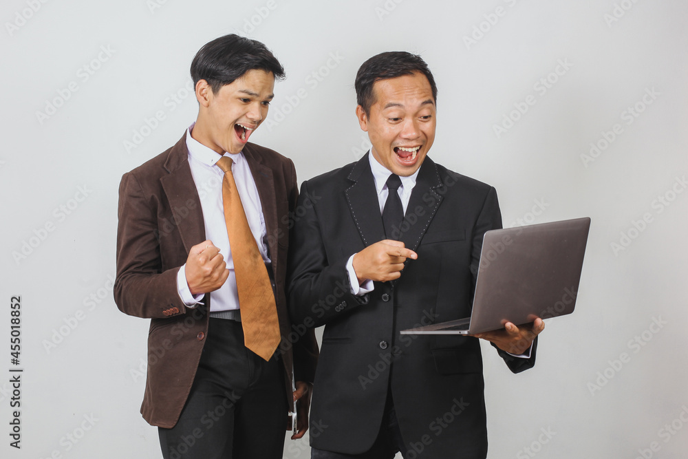 Happy two Asian businessman in suit using a laptop with shocked expression and winning gesture Happy two Asian businessman in suit using a laptop with shocked expression and winning gesture