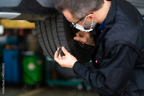 Mechanic checking checking the depth of car tire tread. Car maintenance and auto service garage concept.