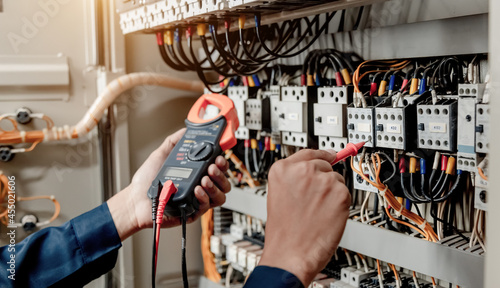 Electrician engineer uses a multimeter to test the electrical installation and power line current in an electrical system control cabinet. photo