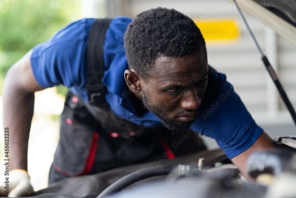 Black male mechanic repairs car in garage. Car maintenance and auto service garage concept. Black male mechanic repairs car in garage. Car maintenance and auto service garage concept.