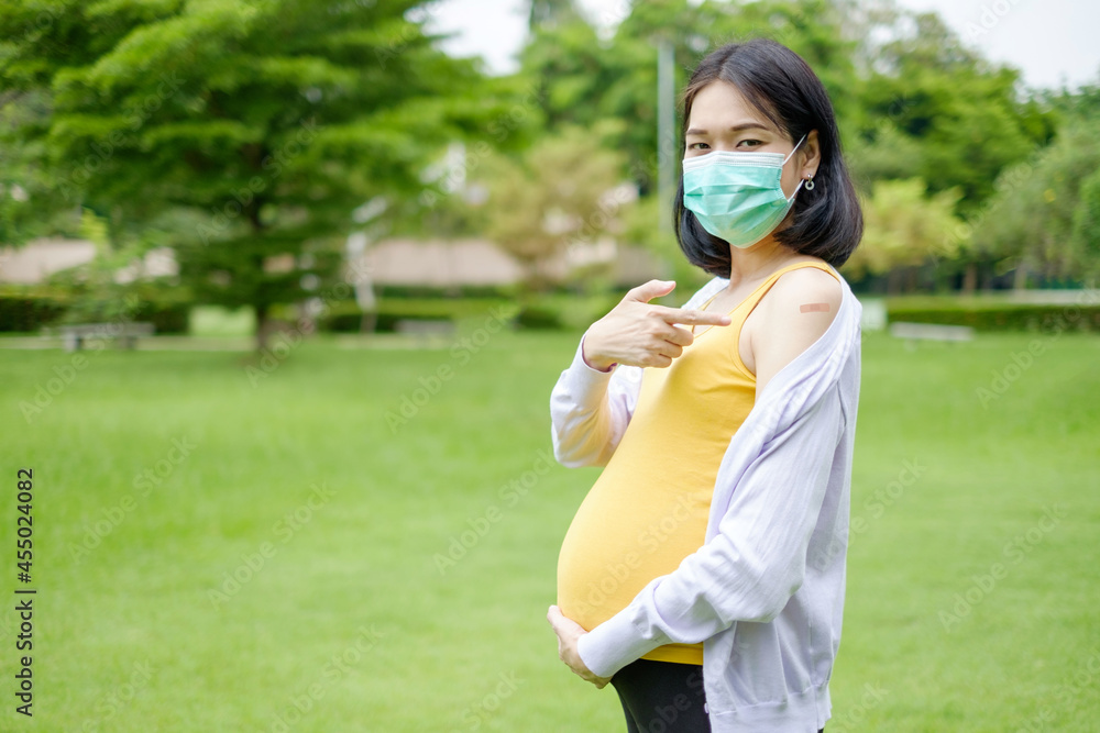 A pregnant mother wearing purple and yellow casual clothes shows finger point plaster on her upper arm after receiving the vaccination. A pregnant mother wearing purple and yellow casual clothes shows finger point plaster on her upper arm after receiving the vaccination.